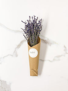 Lavender bunch wrapped in brown kraft paper with a SKIM Ceramics sticker. Staged on a white and gray background.